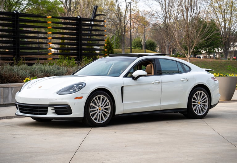 White Porsche Panamera sedan parked in front of wooden fence and landscaping in outdoor setting