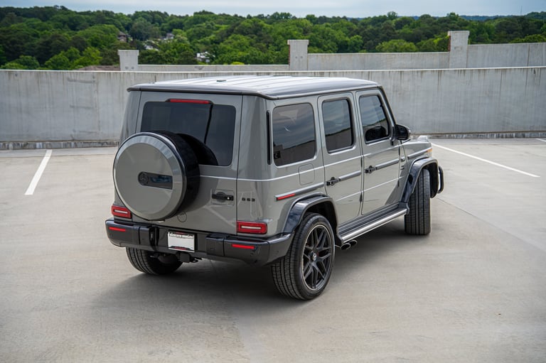 Silver Mercedes-AMG G-Class SUV parked on concrete with forested area in background