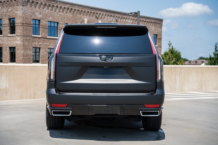 Black Cadillac SUV rear view on parking rooftop with brick building in background