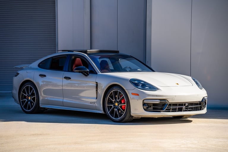 White Porsche sports car parked with drivers door open against modern gray building backdrop