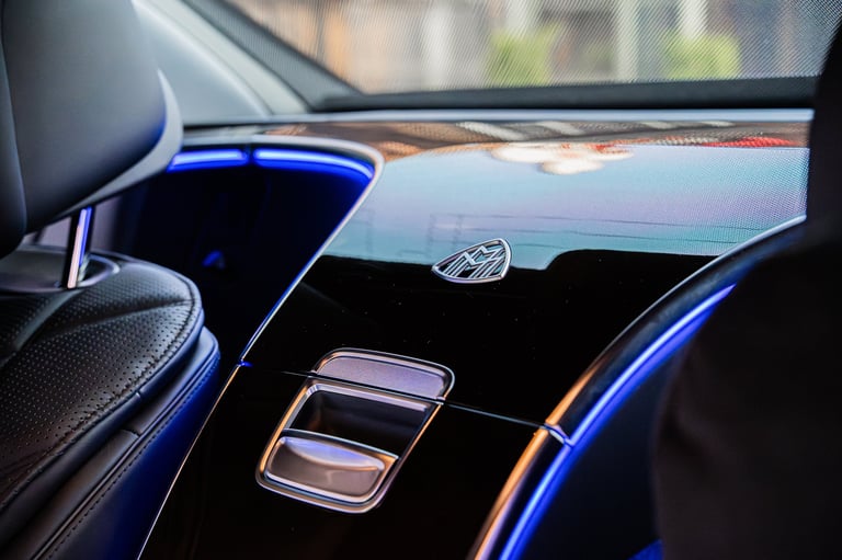 Interior view of luxury car dashboard with blue ambient lighting and modern controls, blurred city background visible through windshield