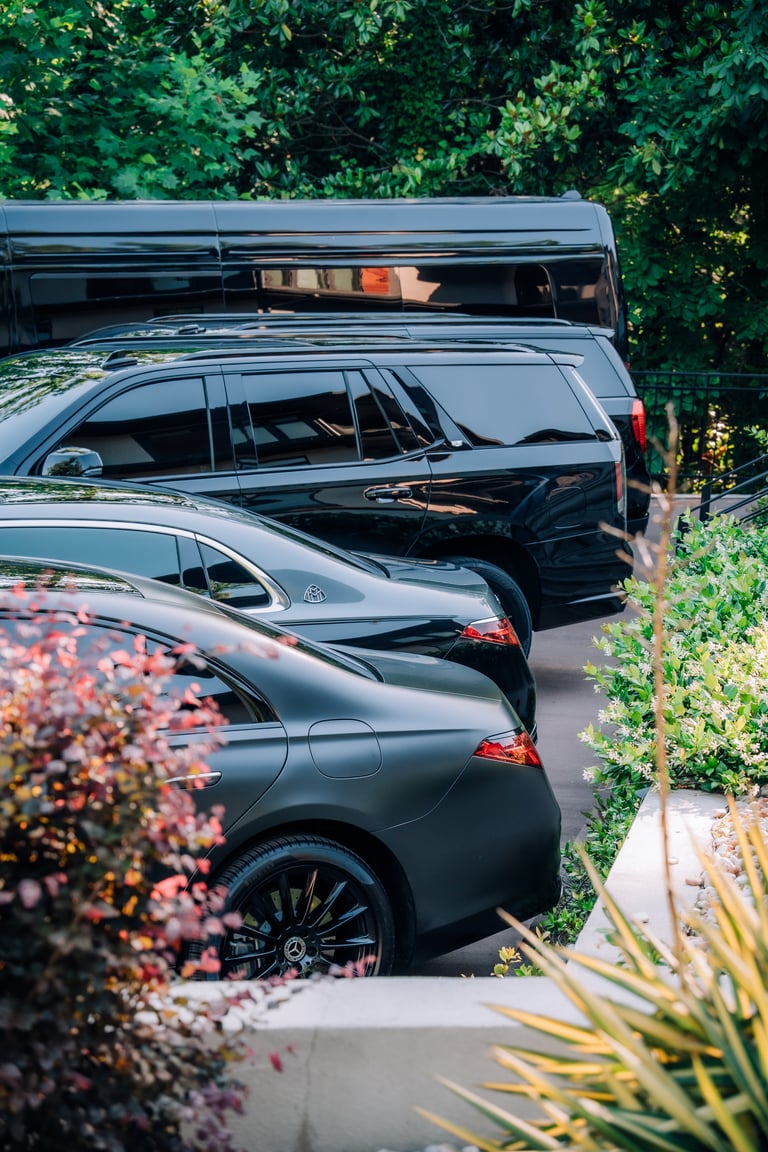 Three luxury vehicles parked in a row beside lush green hedges and flowering plants