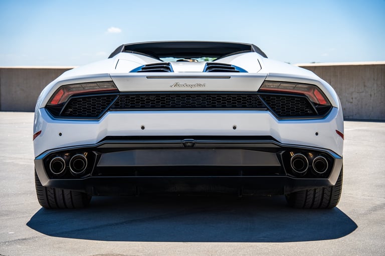 Rear view of a white Lamborghini sports car with dual exhaust pipes in a parking lot