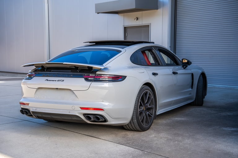 White Porsche Panamera sports car parked in a modern garage, showing rear three-quarter view with sleek design and dark wheels