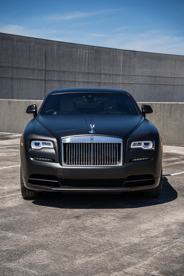 Black Rolls-Royce Wraith luxury coupe photographed from front, parked in concrete garage with blue sky