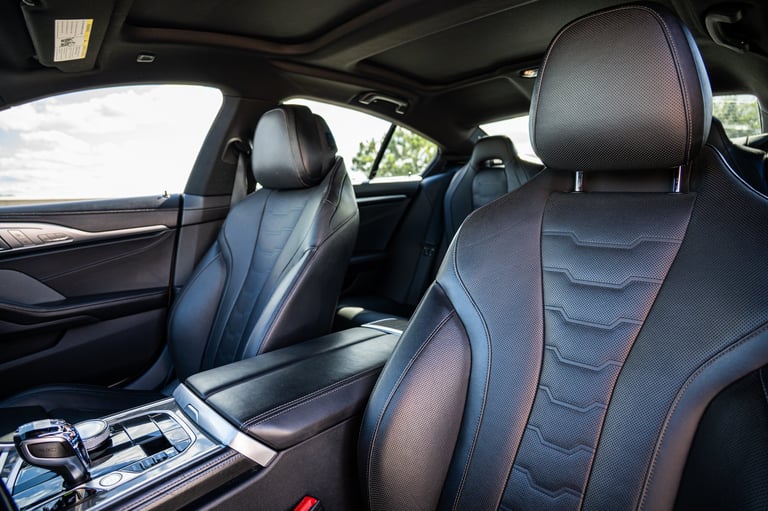 Interior of luxury car with black leather seats, red stitching, and black dashboard visible through front window