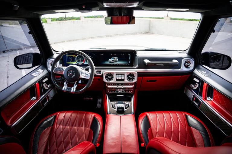 Luxury car interior with red leather quilted seats, dark dashboard, and modern steering wheel viewed from drivers perspective.