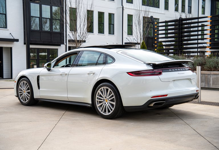White Porsche Panamera luxury sedan parked on a concrete driveway in front of modern architecture