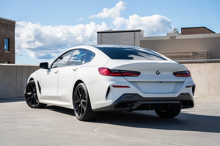 White BMW 8 Series sedan parked on a rooftop, rear three-quarter view in daylight with urban backdrop