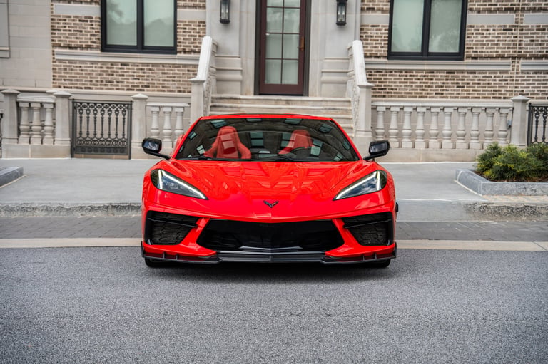 Red sports car parked in front of brick building with white trim and decorative balustrade