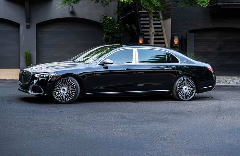 Black luxury sedan parked in driveway with black garage doors and ivy-covered wall in background