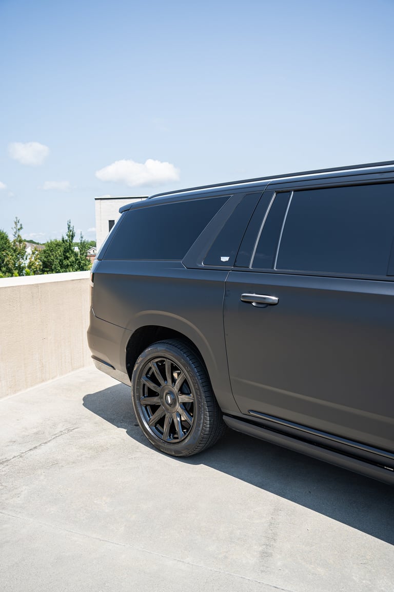 Black luxury SUV parked on concrete surface with alloy wheels, blue sky and trees visible in background