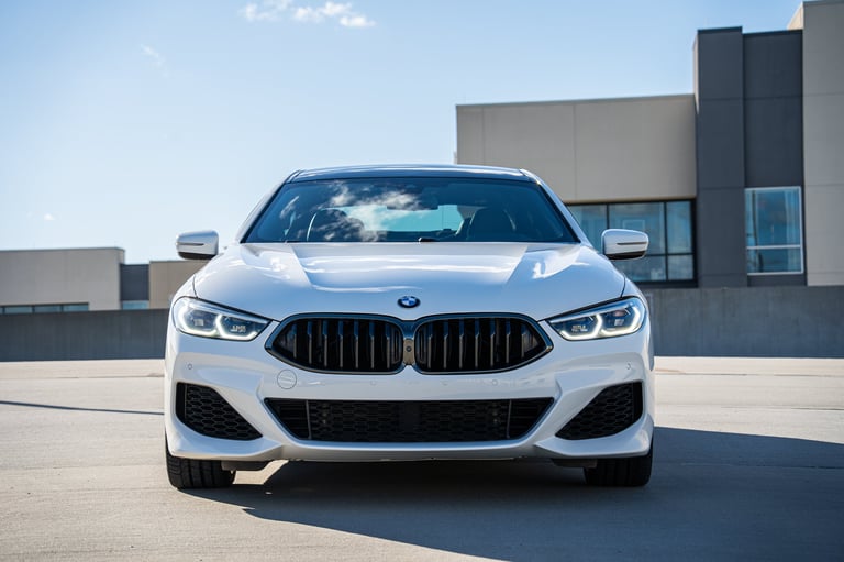 White BMW 8 Series sedan parked on a rooftop, front view with grille detail and modern architecture in background