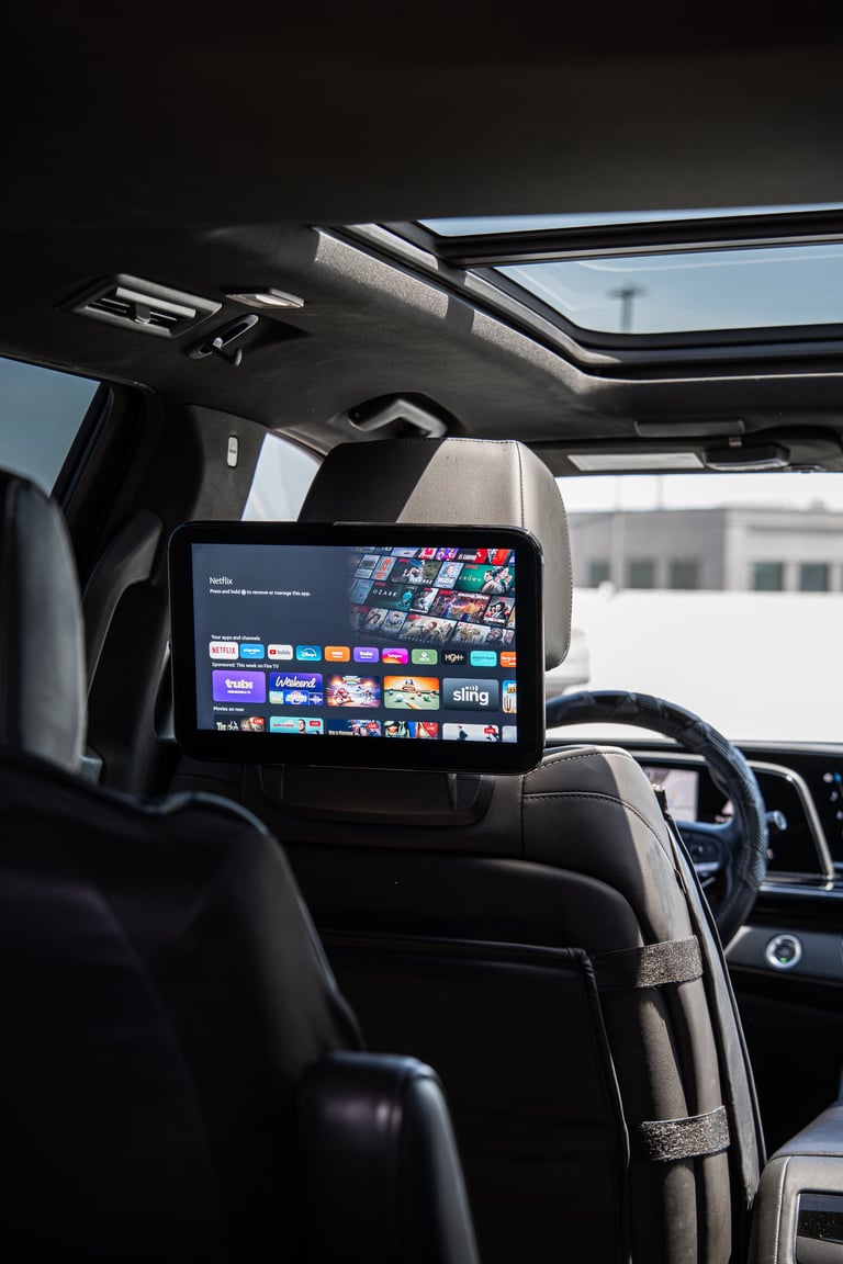 Tablet mounted on car headrest displaying streaming service apps with dark interior and sunroof visible