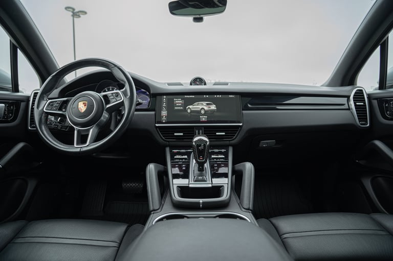 Interior view of a Porsche vehicle showing steering wheel, dashboard with digital display, center console, and leather seats