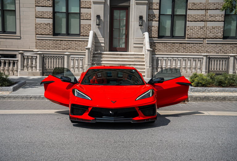 Bright red sports car with open gull-wing doors parked in front of a brick building