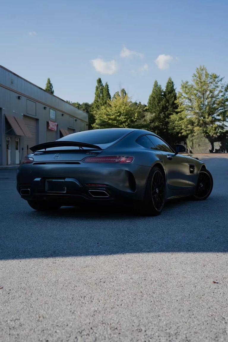 Black sports car parked in lot with industrial building and trees in background