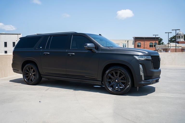 Black Cadillac Escalade SUV parked on a rooftop with industrial buildings in the background under clear blue sky