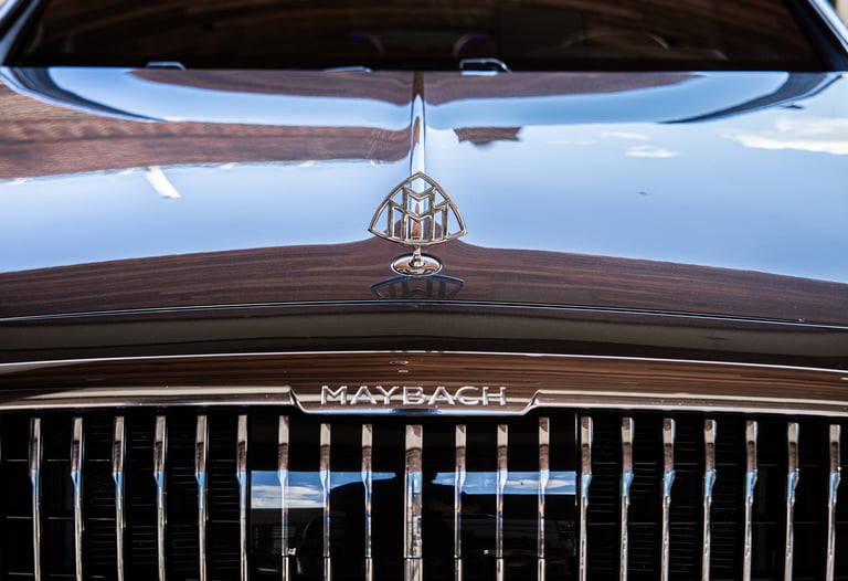 Close-up of vintage Maybach car hood and grille with ornamental mascot and reflective chrome details against blue sky