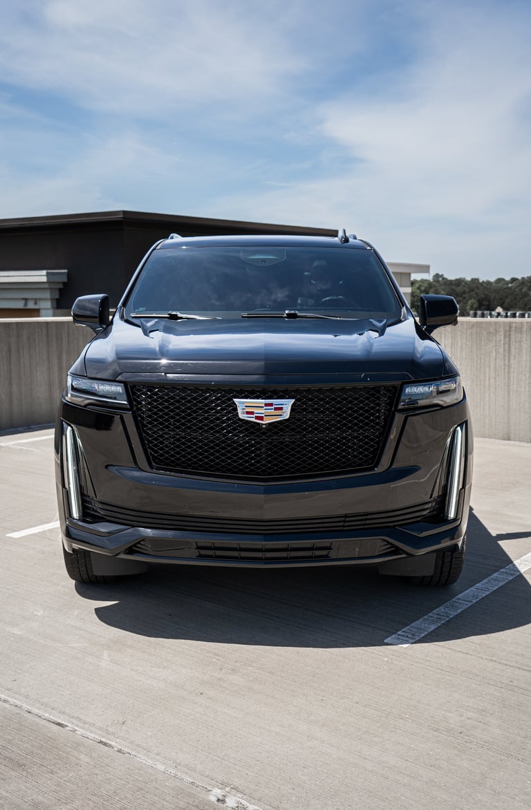 Front view of a black Cadillac Escalade SUV parked on a concrete surface with a building in the background