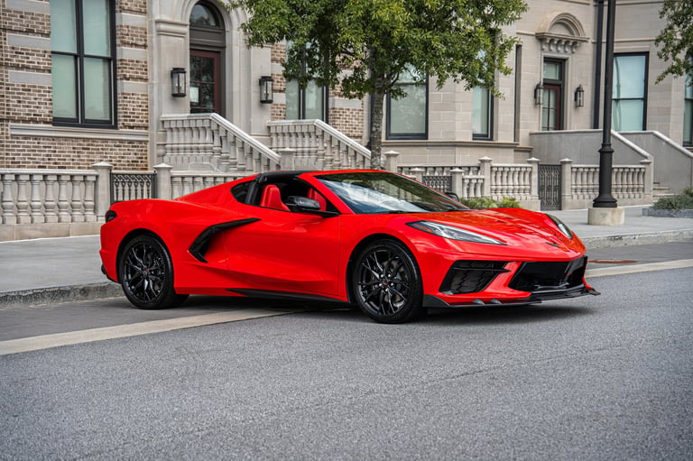 Bright red sports car parked on street in front of classical brick building with columns