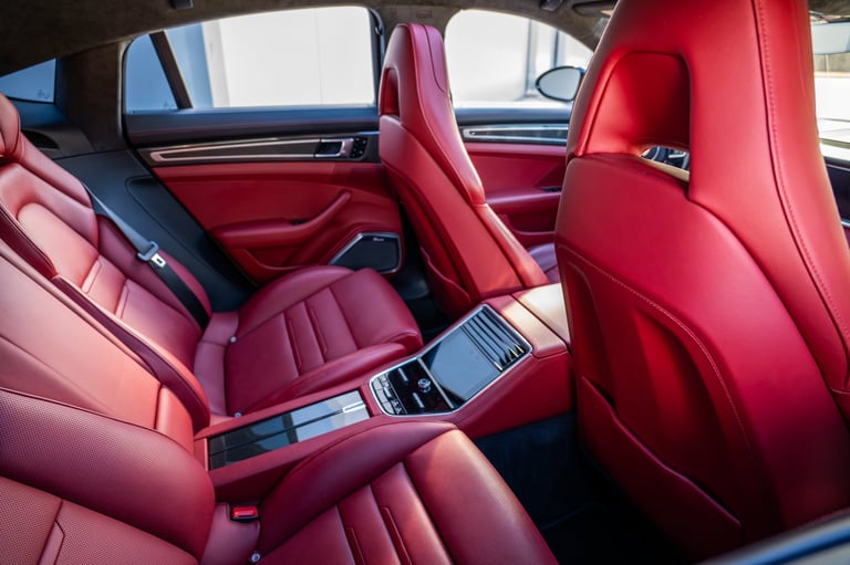 Red leather interior of a luxury car showing quilted seats, console, and windows with natural light