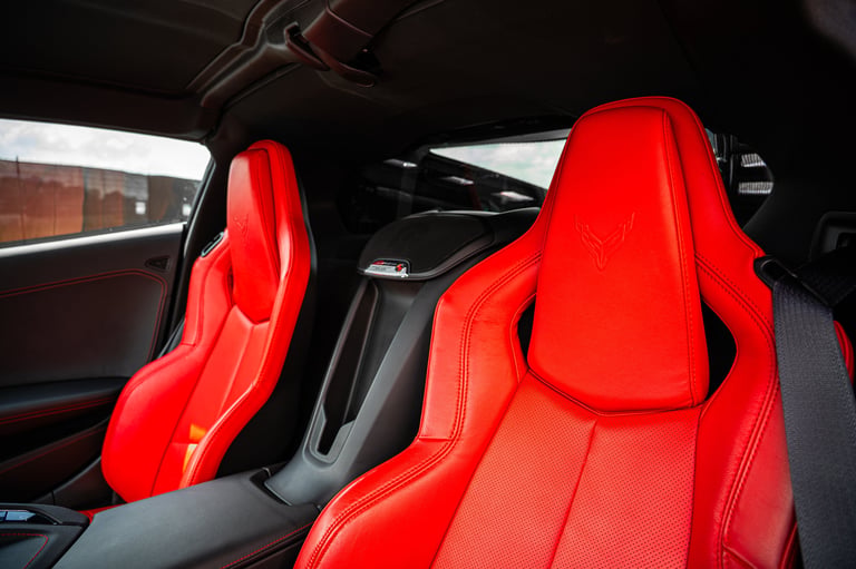 Interior view of a sports car showing two bright red leather bucket seats and black dashboard with sunlight coming through the windshield