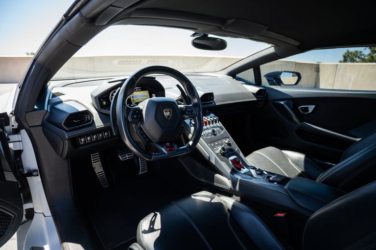 Interior of a luxury sports car with black leather seats, steering wheel, and dashboard with convertible top open.