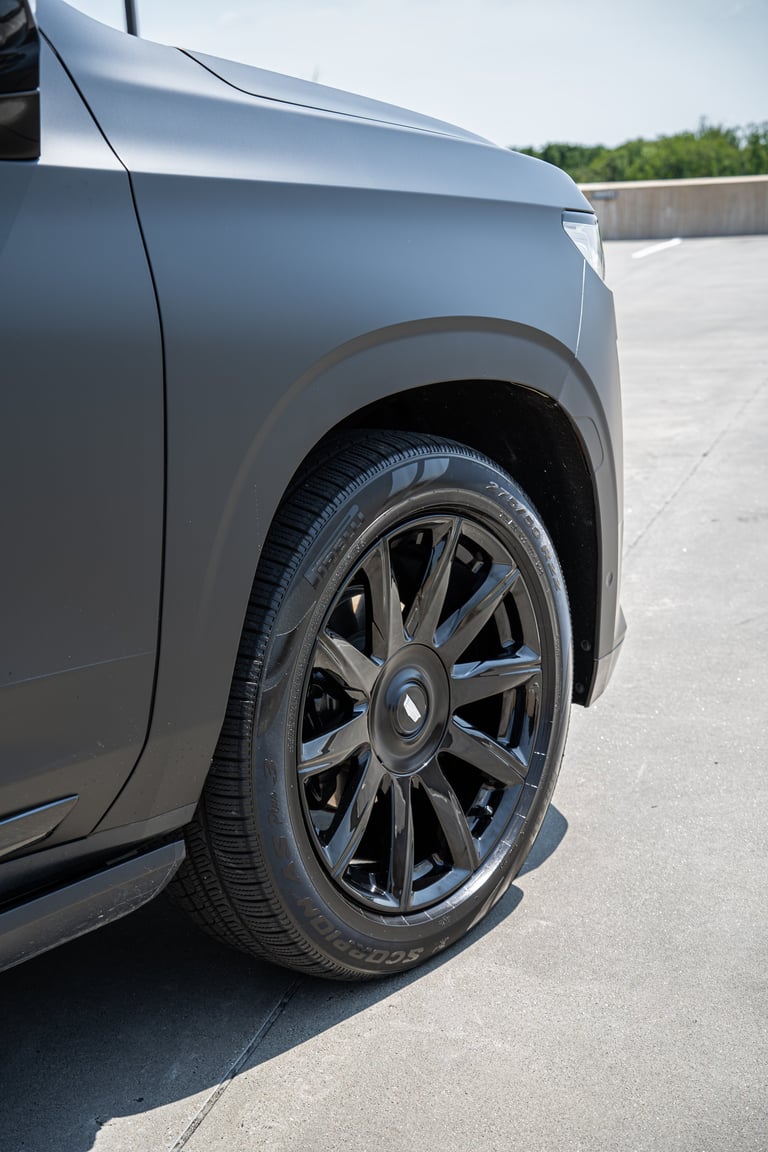 Close-up of a silver SUVs front wheel and tire with dark alloy rim on a concrete surface
