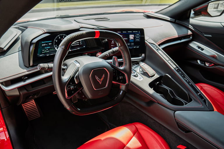 Modern sports car interior with red and black leather seats, steering wheel with red accents, and digital dashboard display.