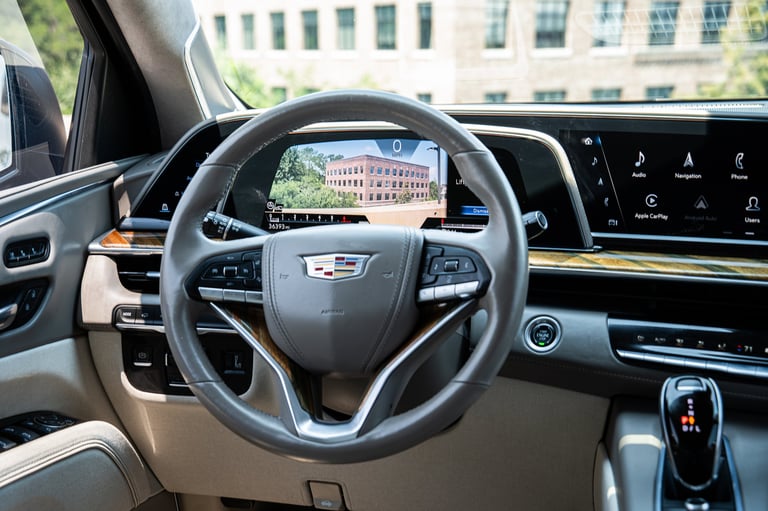 Interior view of a luxury car dashboard showing steering wheel, digital display, and windshield view of a city building