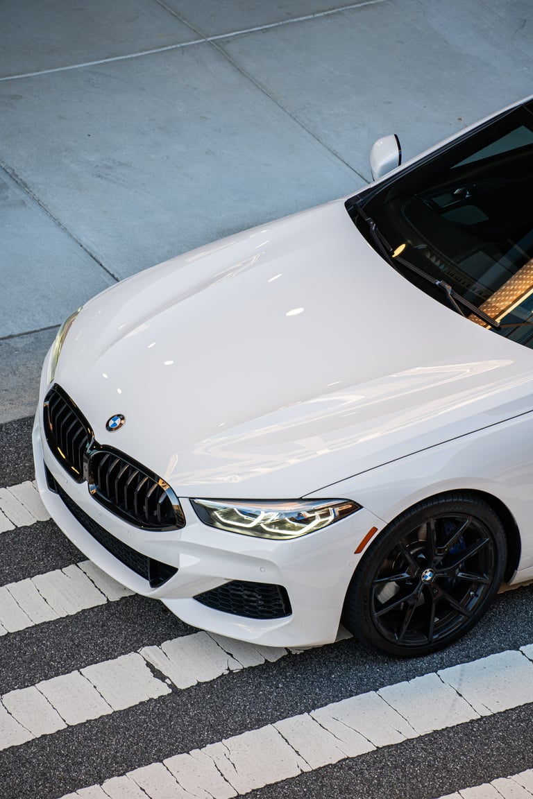 White BMW sedan parked on crosswalk with black grille and dark alloy wheels, overhead view